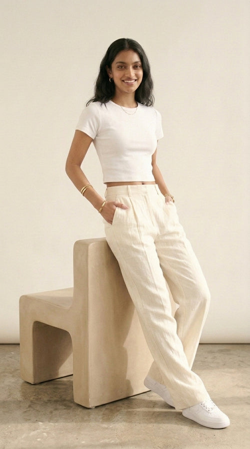 Hallberd Crop Top in white, leaning on a stone seat, styled with cream linen trousers