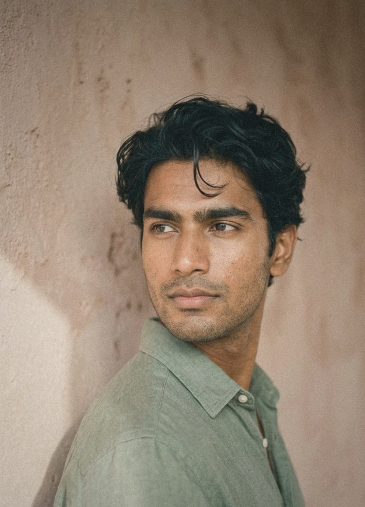 Man in a sage linen shirt against a clay-pink wall, looking away