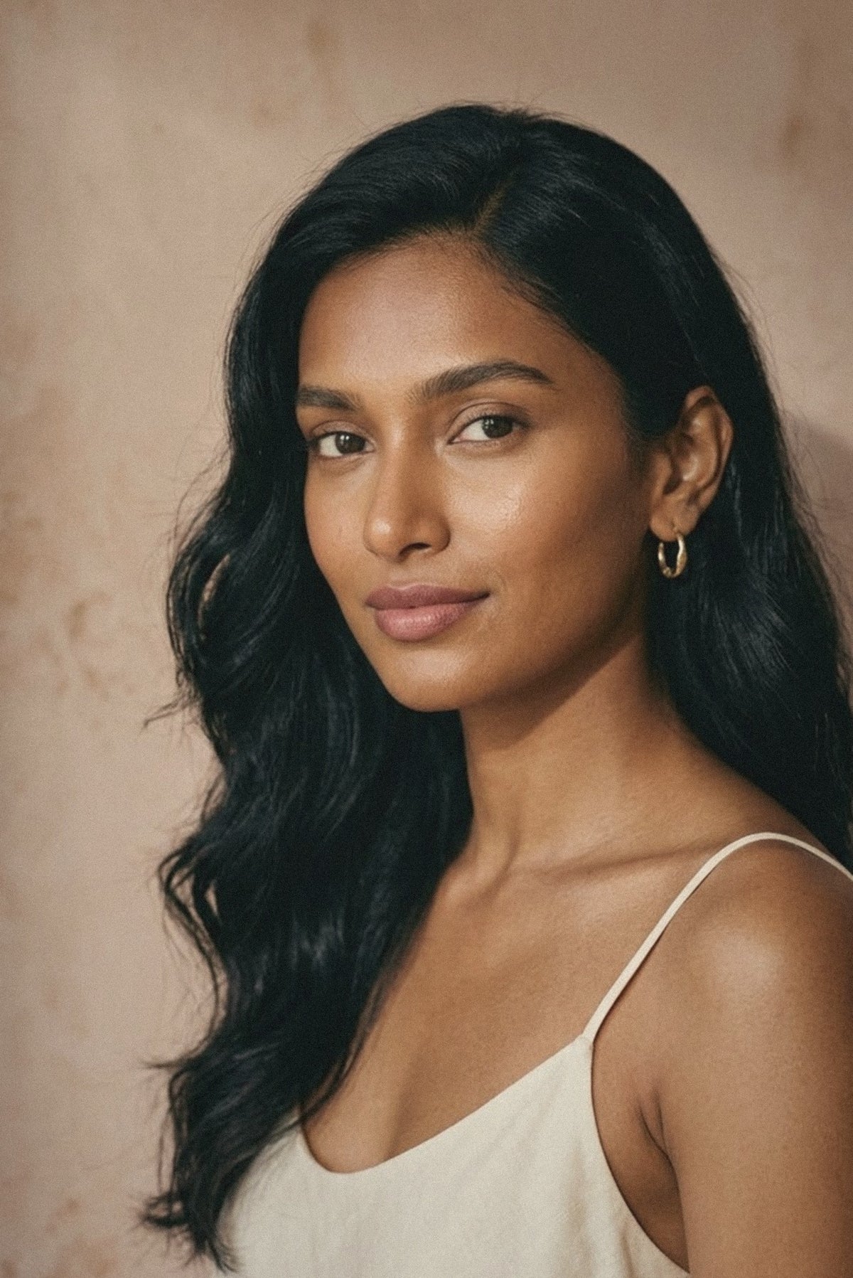 Woman with long dark hair in a cream camisole against a clay-pink wall