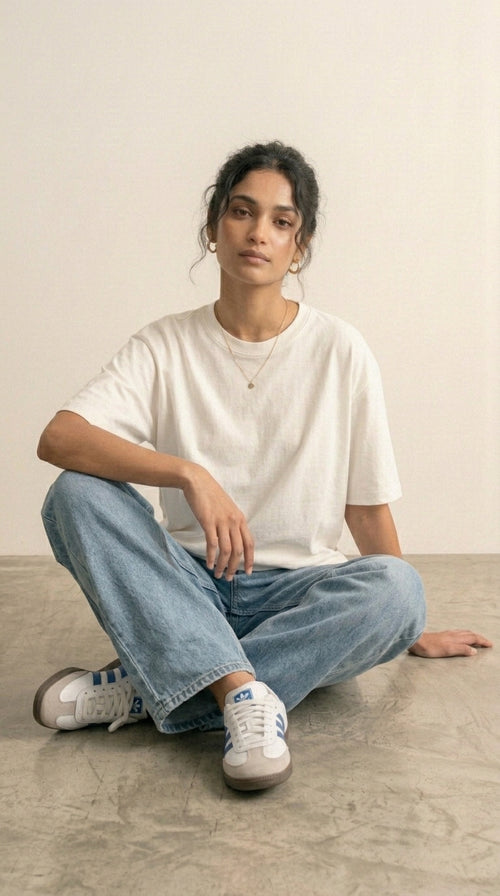 Hallberd Women's Oversized T-Shirt in white, seated on the floor, styled with light-wash jeans